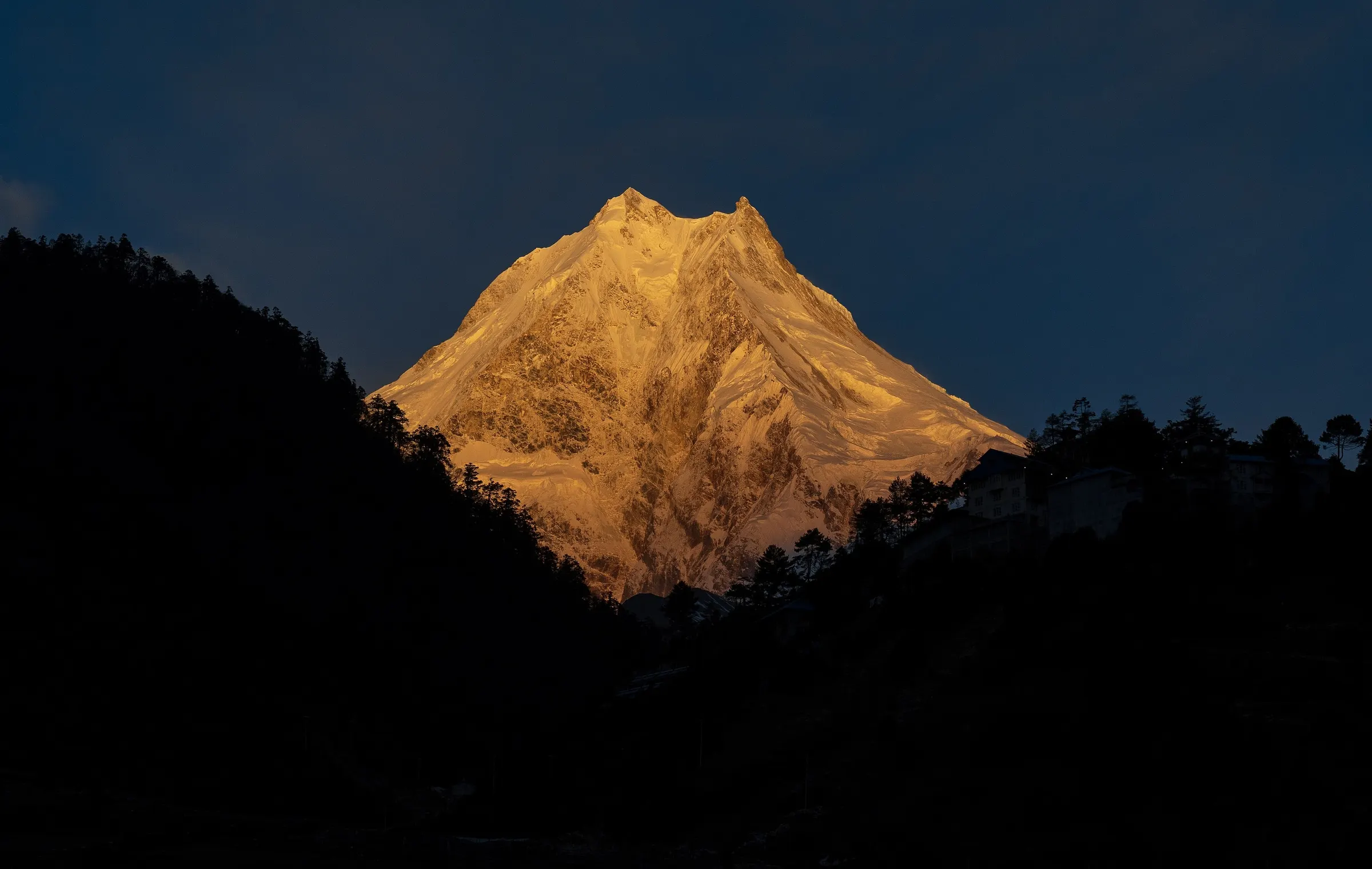 Manaslu glowing orange at sunrise above dark ridges in the Manaslu Conservation Area